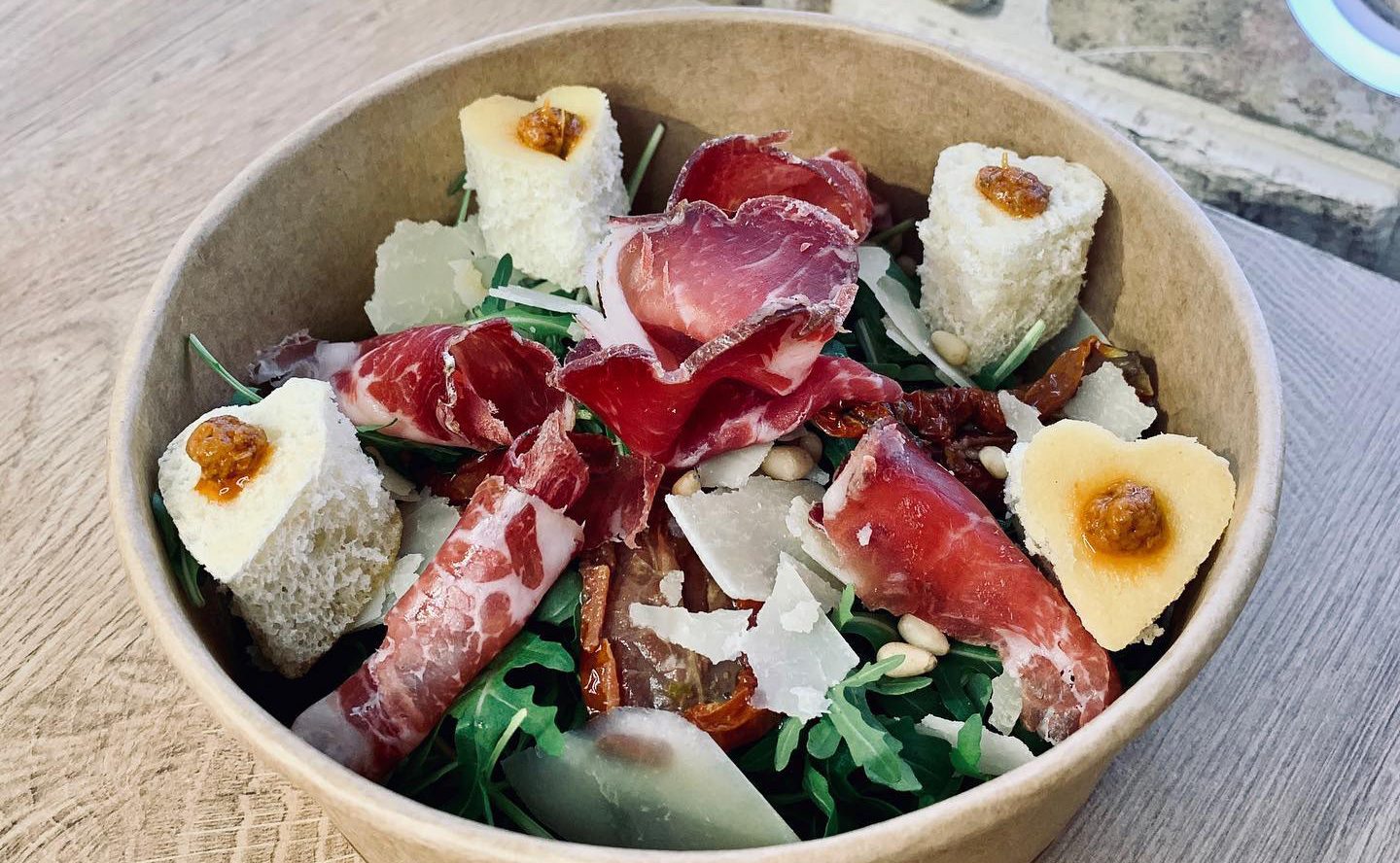 Un bol de salade garnie de jambon cru, de fromage frais et de roquette
