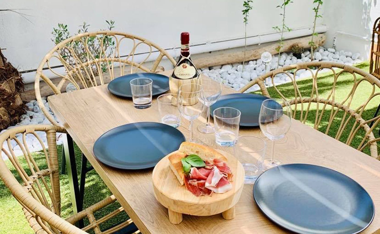 Une table dressée au jardin, avec une bouteille de vin et une petite planche de charcuterie