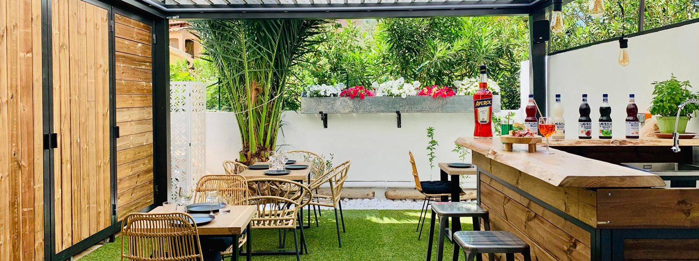 La terrasse-jardin de l'épicerie : tables en bois, chaises en rotin, comptoir et plantes